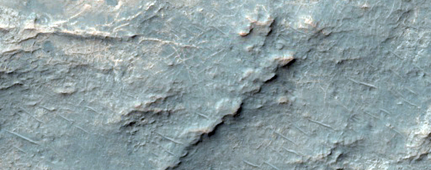 Afloramentos brilhantes e escuros cortados por um canal na Cratera Savich